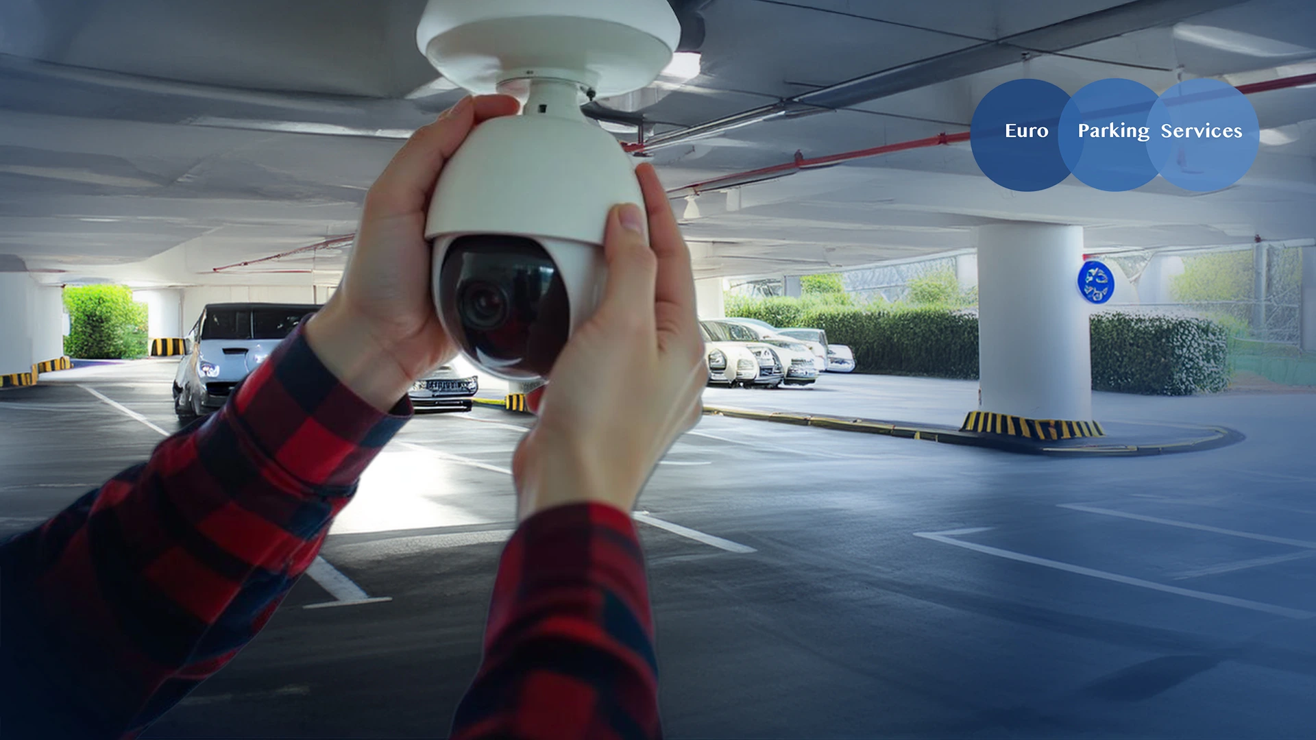 A person installs a CCTV camera on the ceiling of a parking space.