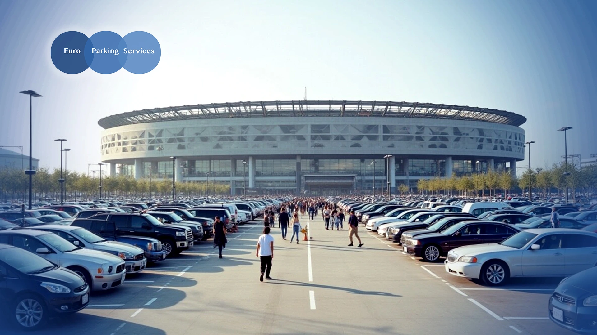 A large stadium with a modern design and spacious, well-organised car park filled with various vehicles.