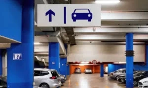 Underground parking space with blue pillars, parked cars, and a directional sign showing a car and an arrow pointing forward